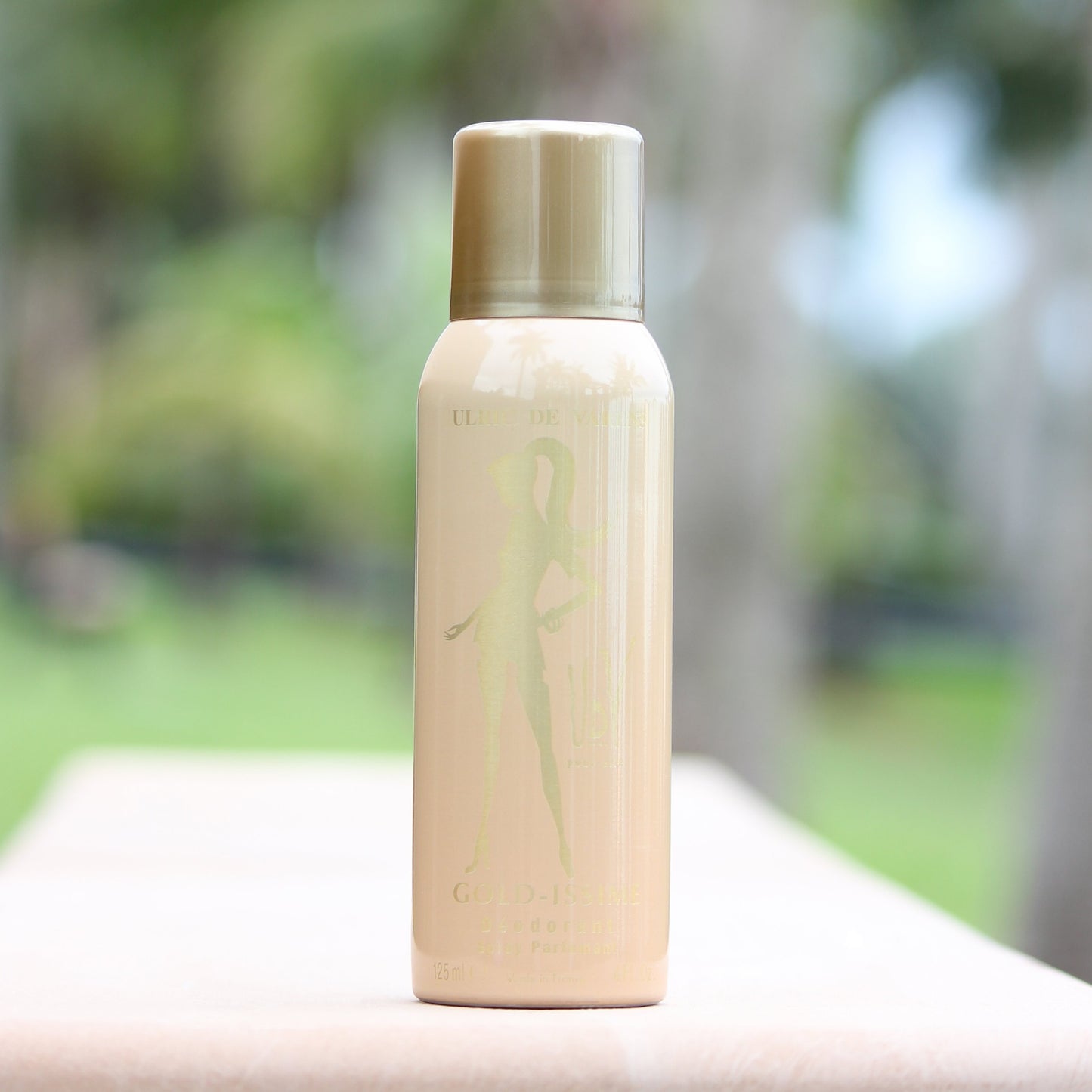 Ulric De Varens Gold-issime women's perfume scented deodorant 4 oz in front of trees.
